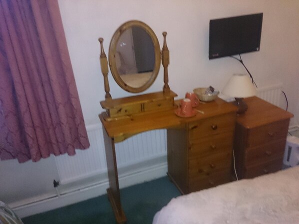 A bedroom with a wooden dresser, a mirror, a television on the wall, and a bed.