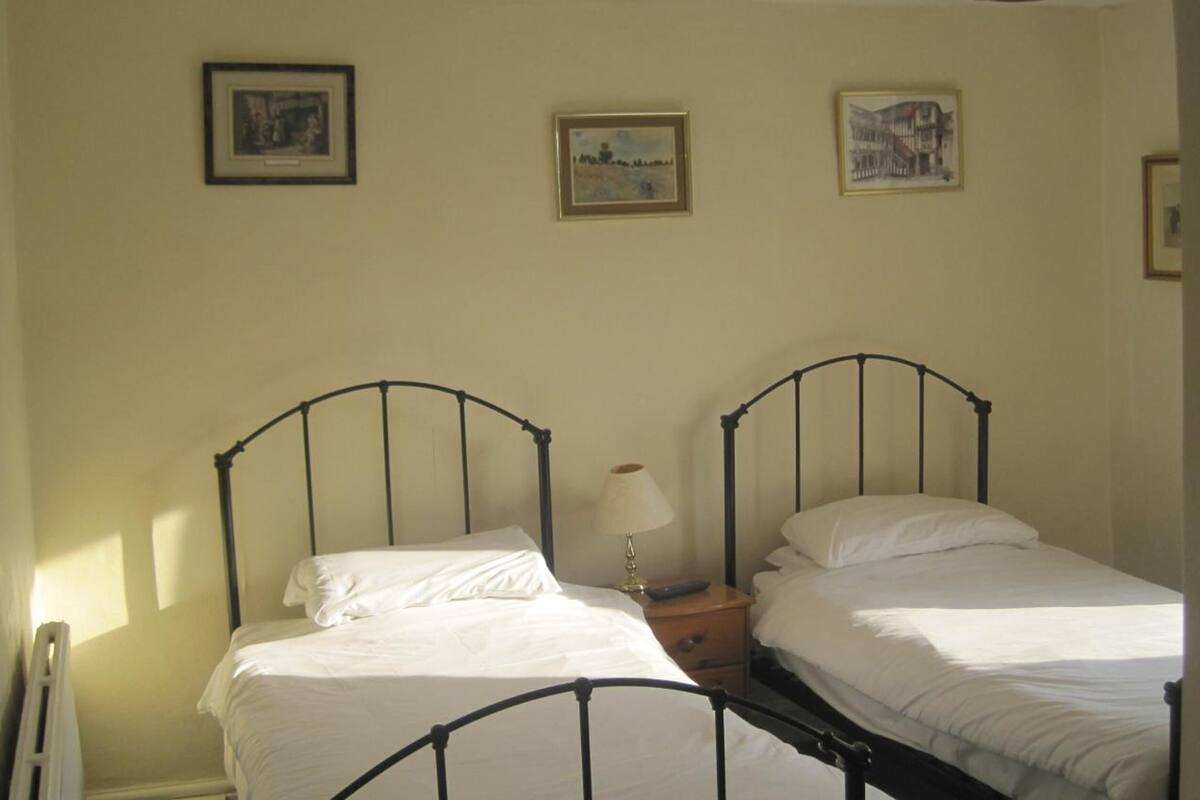 A room with two single beds, a bedside table with a lamp, and three framed pictures on the wall.