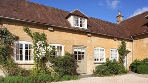 A stone building with a tiled roof, a central entrance door, and three windows on the ground floor. - Saratoga Cottage (Chipping Norton)
