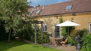 A stone building with a tiled roof, a patio with a table and chairs, and a grill. - Saratoga Cottage (Chipping Norton)