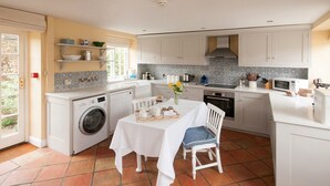 A compact kitchen with a washing machine, a dining table with chairs, and a microwave. - Saratoga Cottage (Chipping Norton)