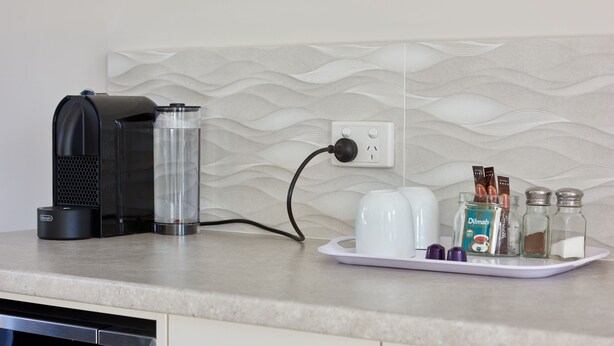 Een keukenblad met een koffiezetapparaat, een waterdispenser, een witte schaal met zout- en peperstrooiers, en een pot koffiepads.