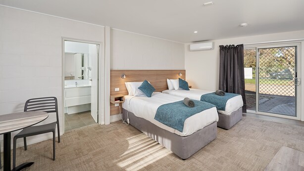 Quarto de hotel moderno com duas camas, uma escrivaninha e um banheiro.