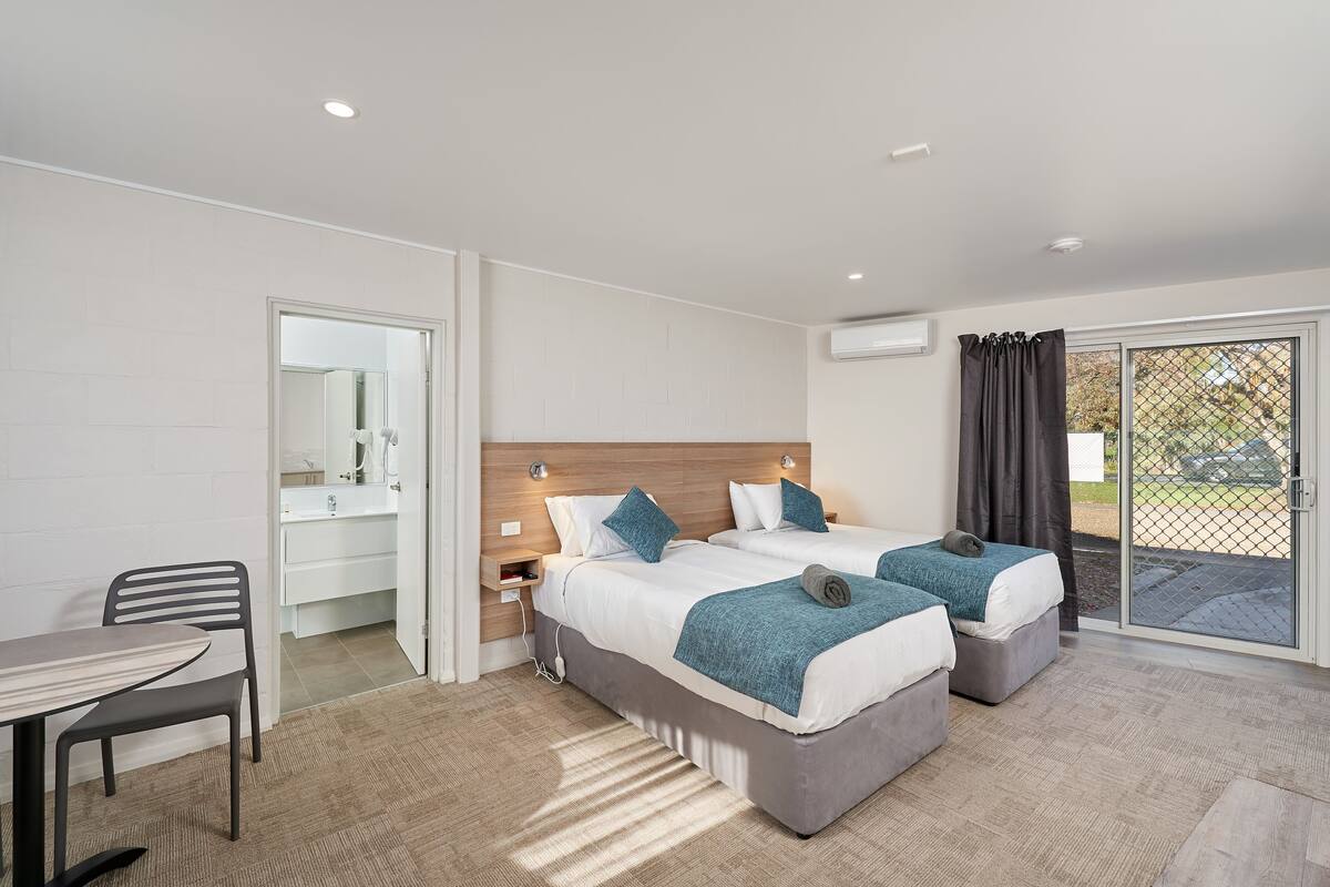 A modern hotel room with two beds, a desk, and a bathroom.