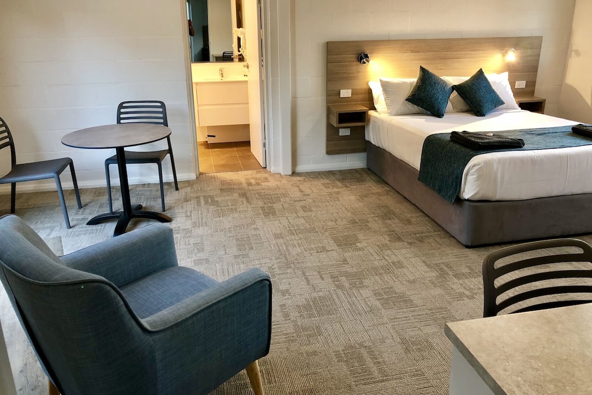 A hotel room with a bed, two chairs, a small table, and a bathroom visible through an open door.