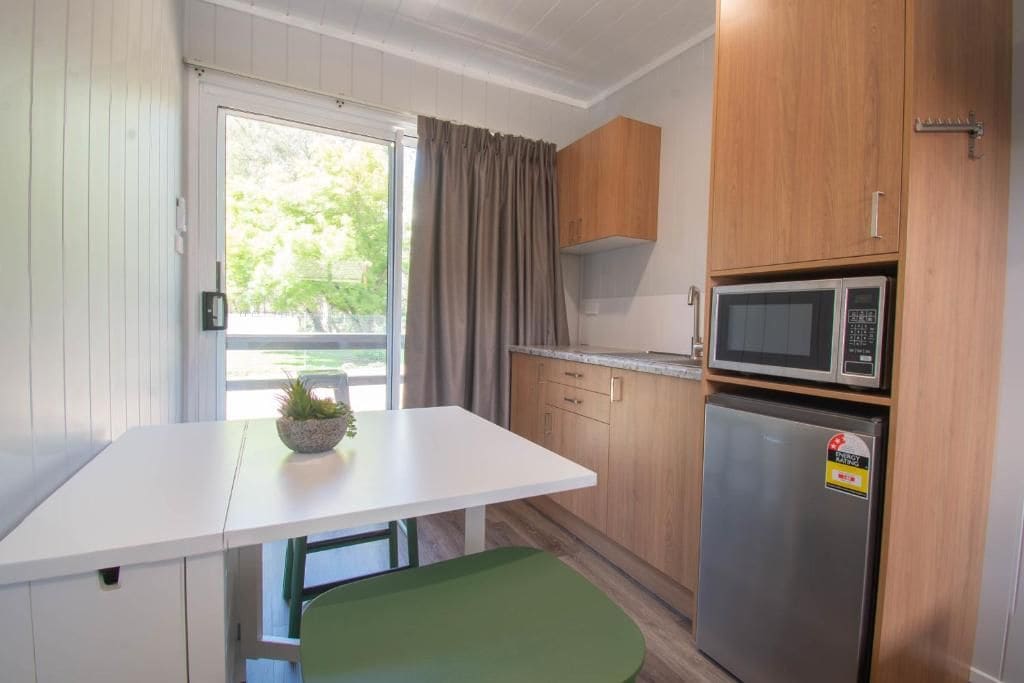 Cozinha compacta com bancada branca, armários de madeira, micro-ondas e geladeira.