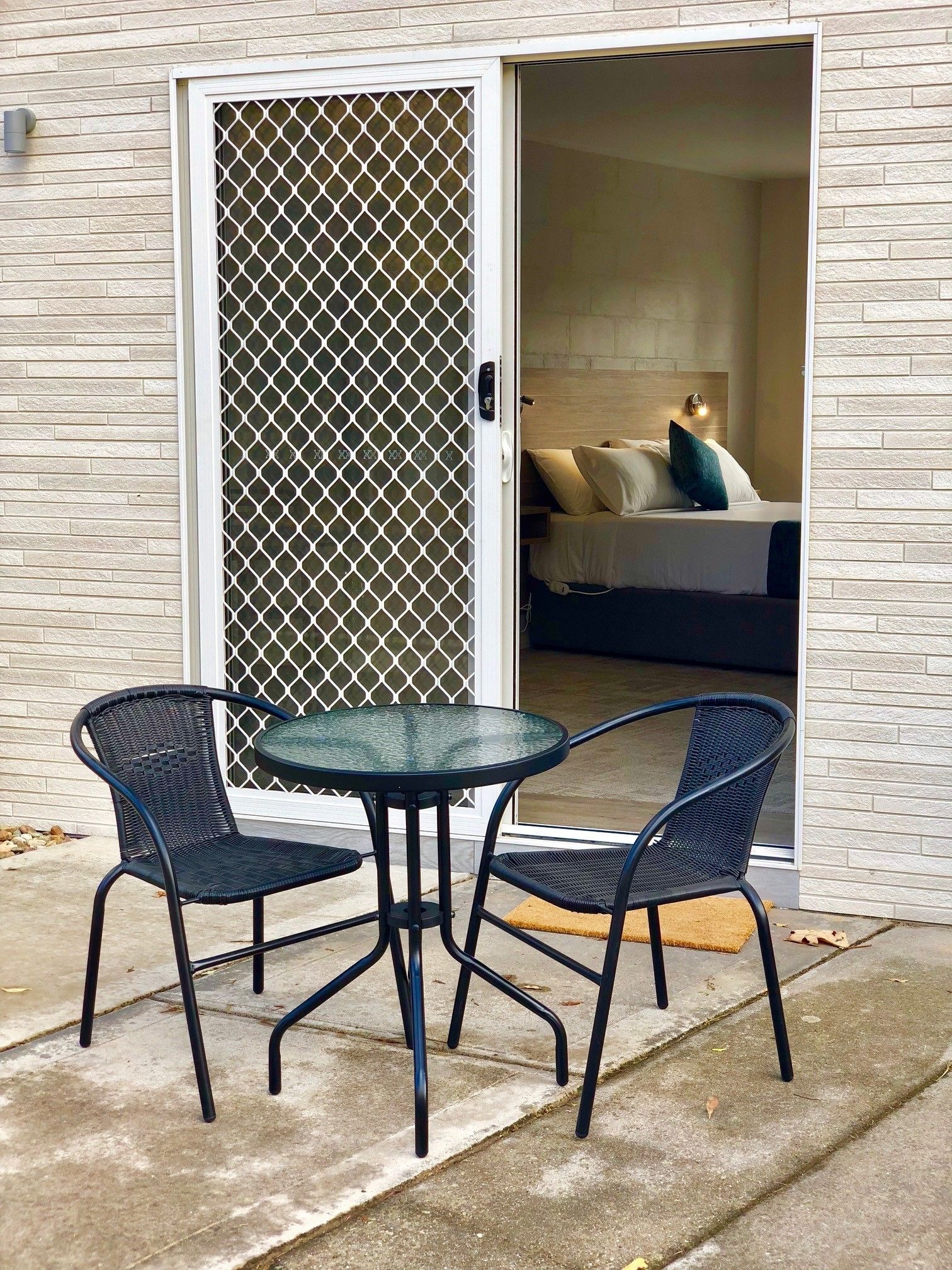 Une pièce comprenant un lit, une fenêtre ornée d’un paravent décoratif et une petite table avec deux chaises.
