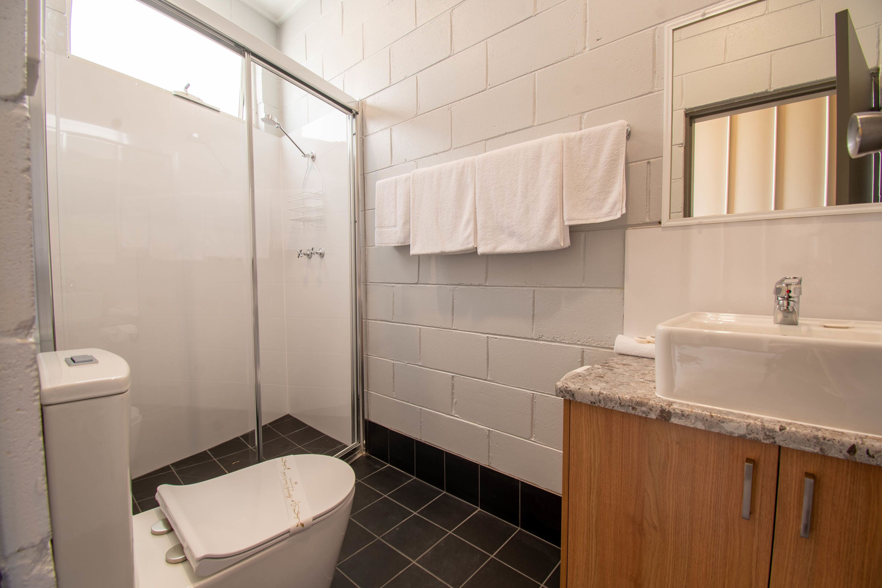 Ein Badezimmer mit Duschkabine, Toilette, Waschbecken mit Spiegel und Handtuchhalter mit mehreren Handtüchern.