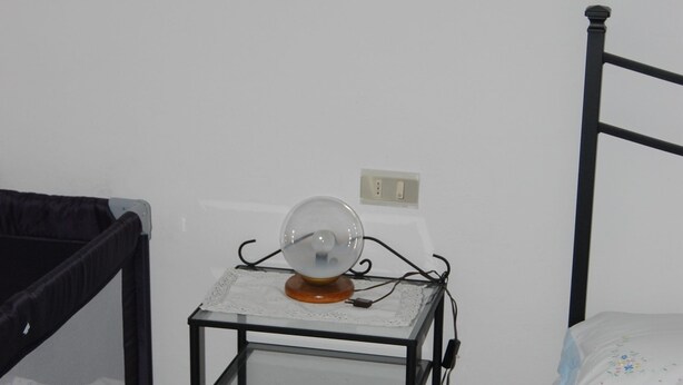Ein kleines Zimmer mit einem Etagenbett, einem Nachttisch mit Ventilator und einer Steckdose an der Wand.