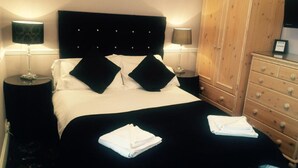 A neatly made bed with black and white bedding, two bedside lamps, a wooden dresser, and folded white towels on the bed. - Broom Lodge (Largs)