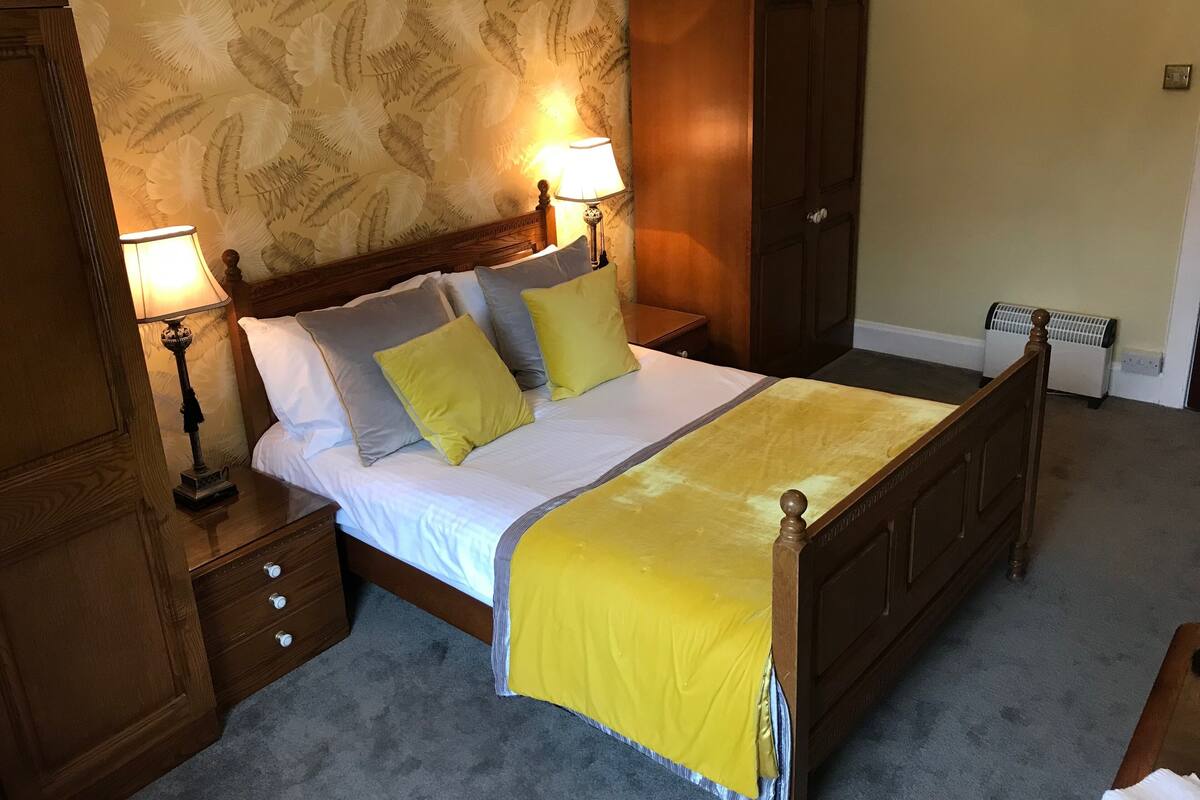 Quarto com cama de madeira, duas mesas de cabeceira com luminárias, um guarda-roupa e um radiador.