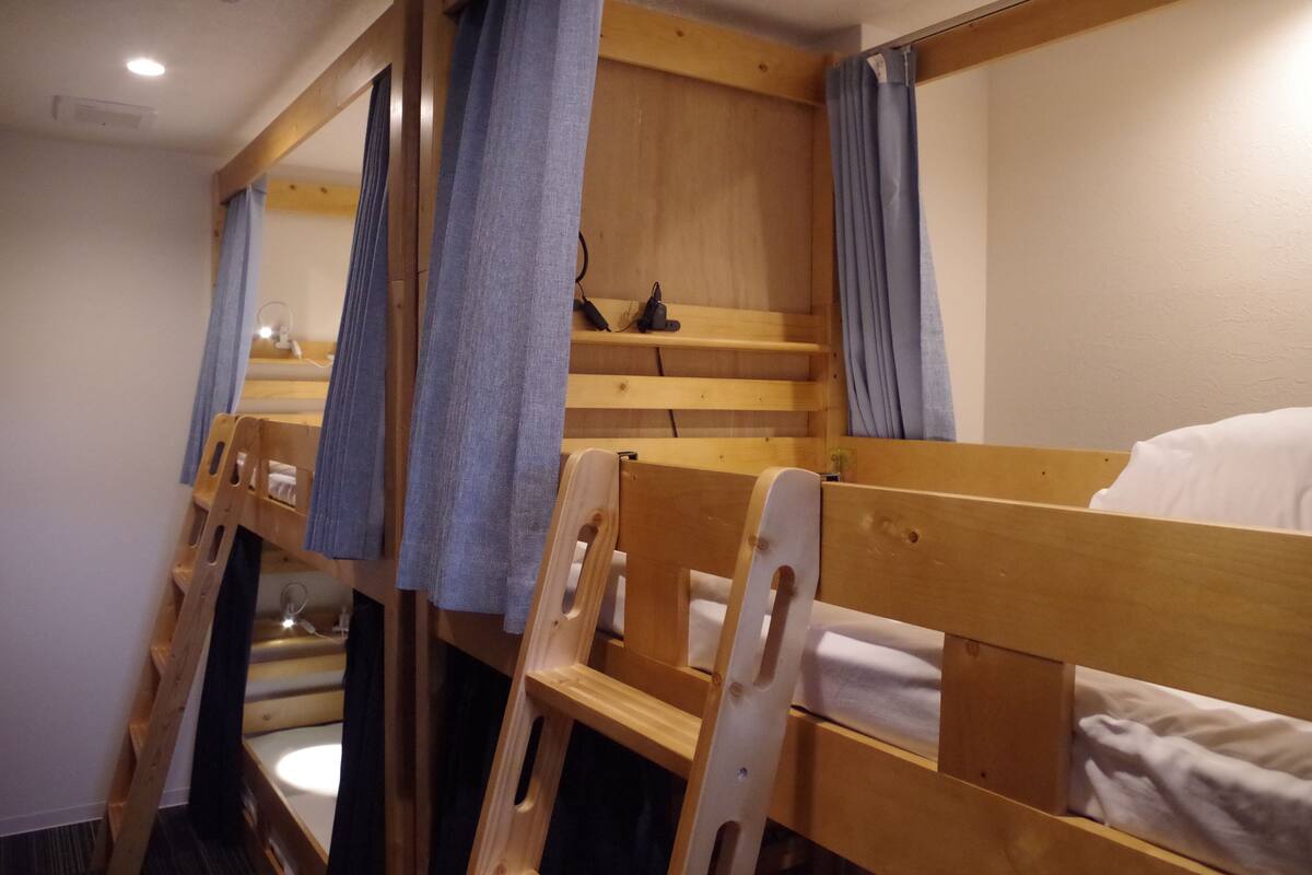 Dormitorio con literas de madera, una pequeña estantería y un espejo.