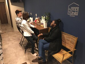 Un grupo de personas sentadas alrededor de una mesa en una habitación con una pared azul oscuro y un logo que dice "The Guest House POP TONE HIROSHIMA".