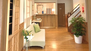 A hallway with a wooden floor, a white sofa with a green pillow, a wooden cabinet with open doors, and a potted plant. - samurise NORTH (Fujikawaguchiko)