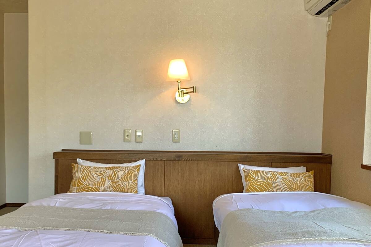 Ein Hotelzimmer mit zwei Betten, einem Holzkopfende, einer Wandleuchte und einem strukturierten Teppich.