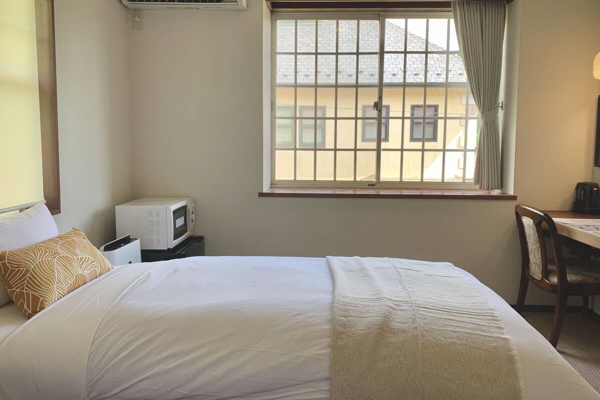 Ein Hotelzimmer mit einem Bett, einem Schreibtisch, einem Sessel, einer Mikrowelle und einem Fenster mit Vorhängen.