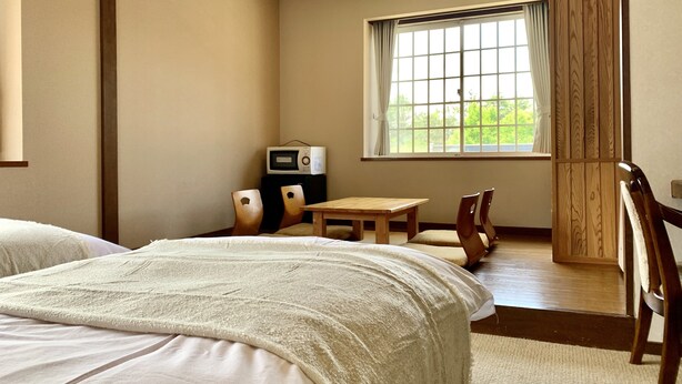 A hotel room with a bed, a small table, a chair, a microwave, and a window with a view of greenery. - samurise NORTH (Fujikawaguchiko)