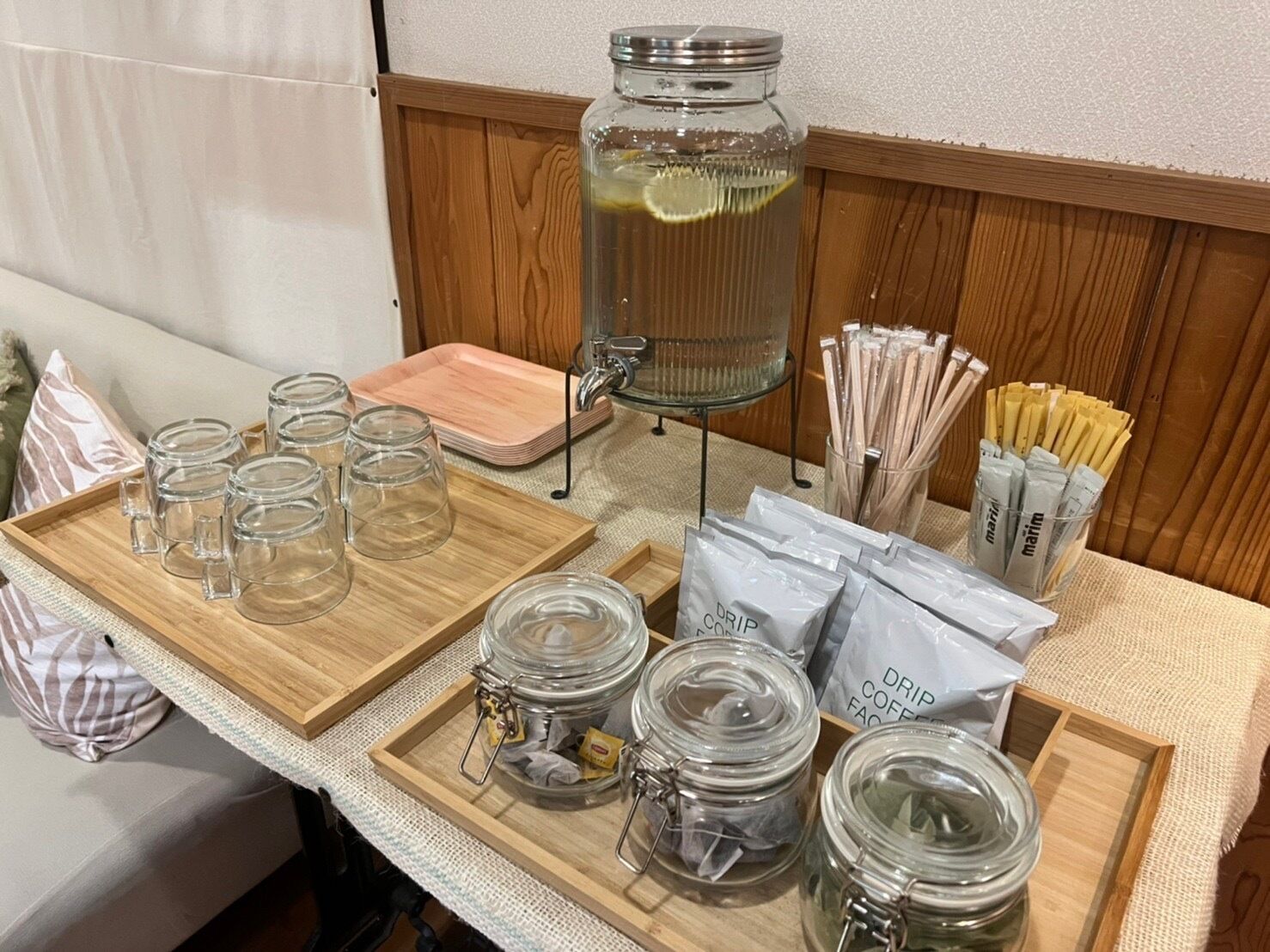 A breakfast setup with glass jars, a pitcher, and tea bags on a wooden tray.