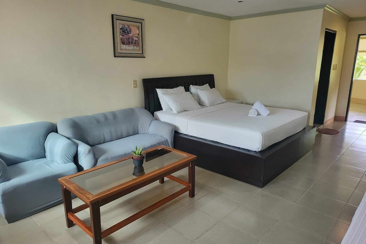 Habitación de hotel con una cama, un sofá, una mesa de centro de madera y un cuadro en la pared.