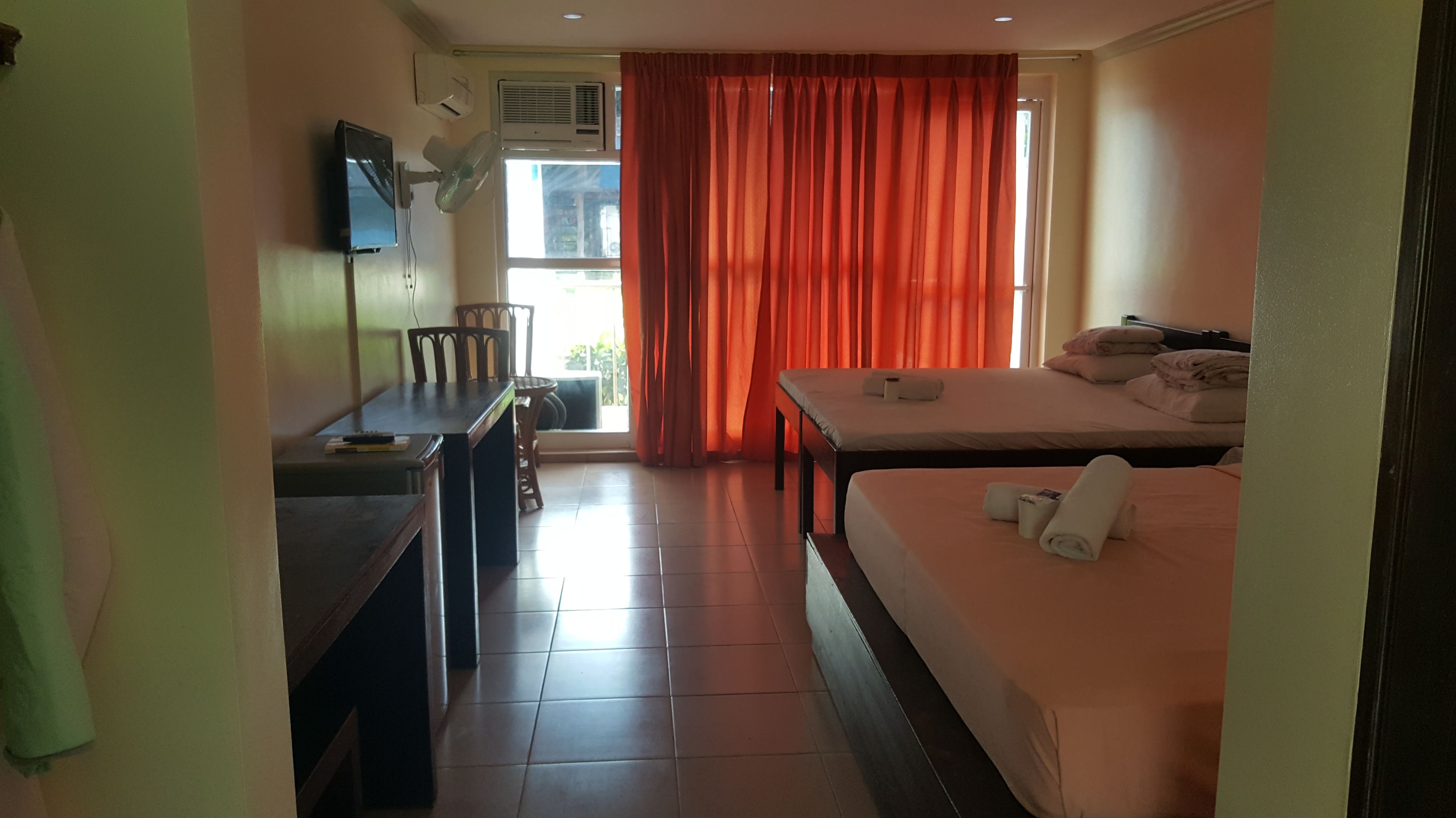 A hotel room with a bed, a desk, a chair, a TV, and a window with curtains.