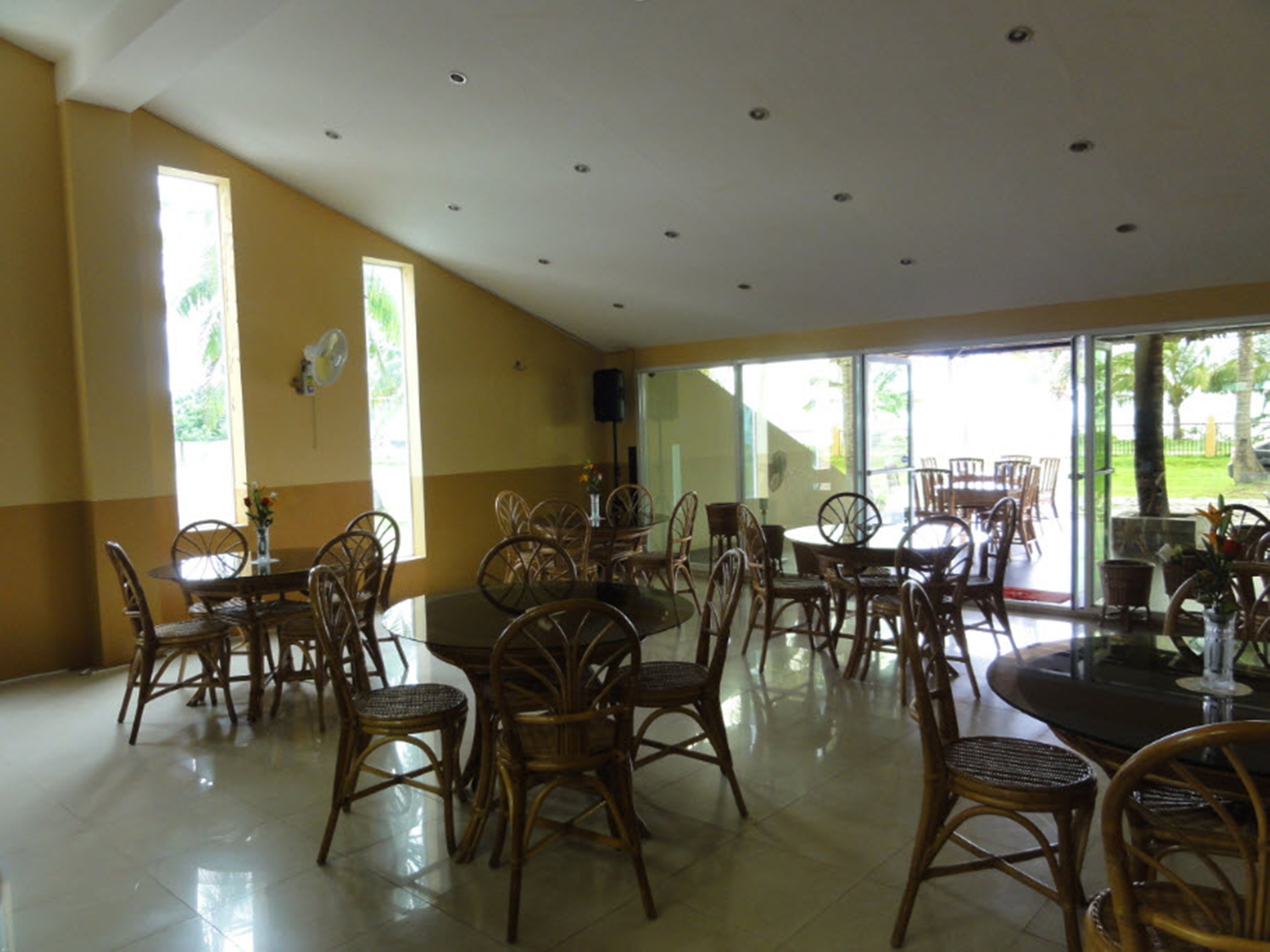 A spacious dining area with wicker chairs and tables, large windows, and a ceiling with recessed lighting.