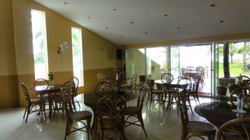A spacious dining area with wicker chairs and tables, large windows, and a ceiling with recessed lighting.