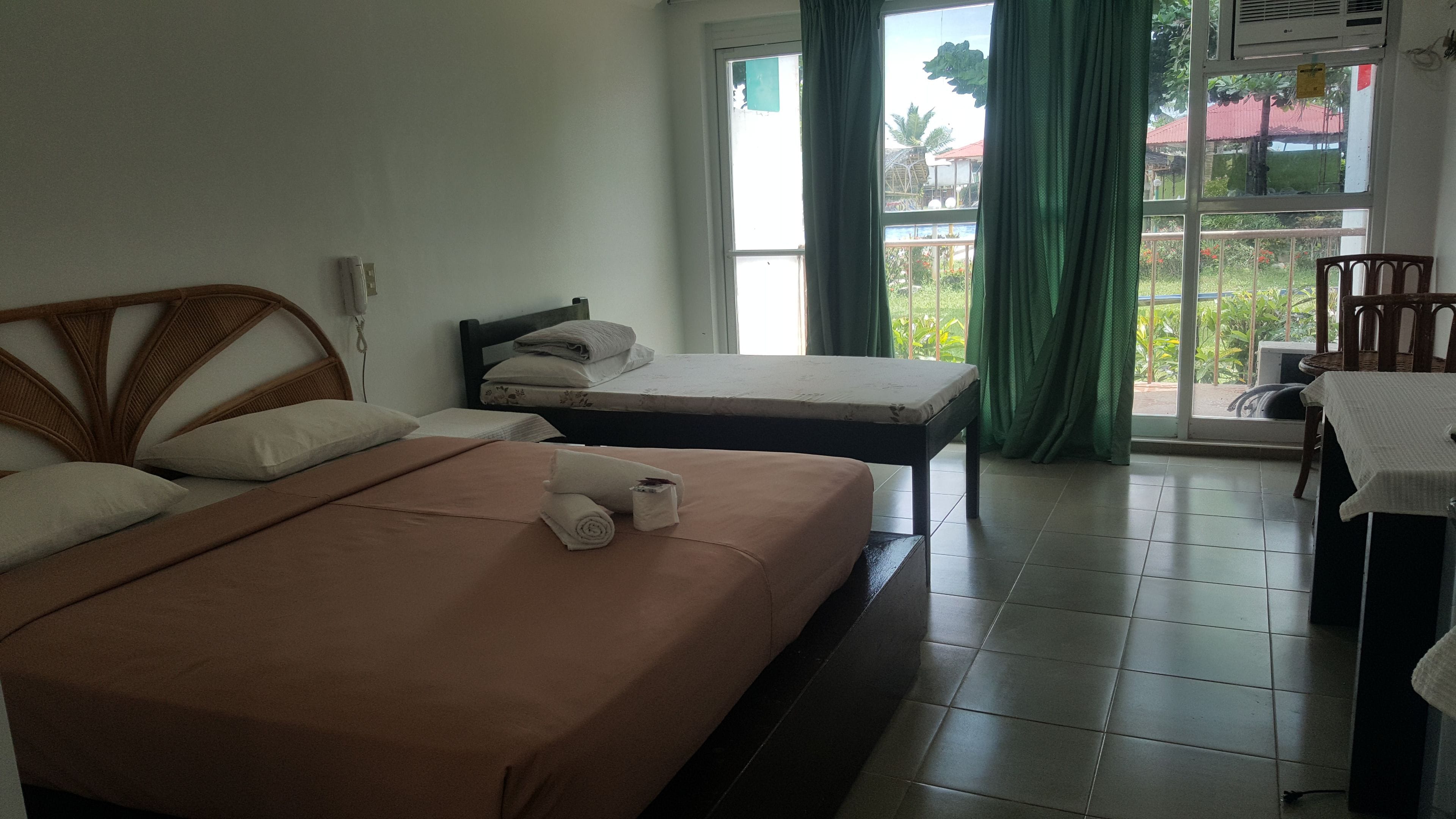 A hotel room with two beds, a small table, and a view of the outdoors through a window.