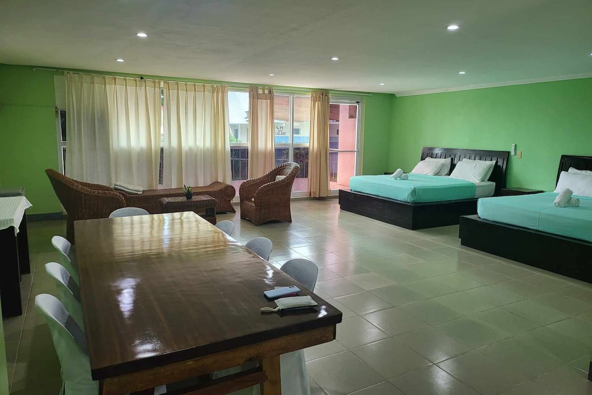 Habitación de hotel con comedor, dos camas y balcón con cortinas.