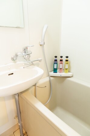 A bathroom with a white sink, a bathtub, and a shelf with three bottles of toiletries.