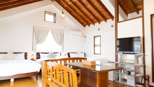 A spacious room with a wooden ceiling, a bed, a desk, and a television. - Pine House in Churaumi (Motobu)