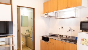 A compact kitchen with wooden cabinets, a stainless steel sink, and a microwave. - Pine House in Churaumi (Motobu)