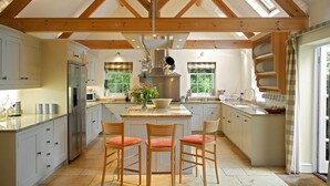A spacious kitchen with wooden beams, a central island, and a large window. - Weir Cottage (Chipping Norton)