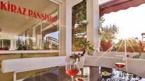 A table with two wine glasses and a small bowl of cherries, a potted plant, and a window with the name "KIRAZ PANSİON" visible.