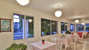 A dining area with tables and chairs, large windows, and potted plants.