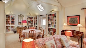 Ein gemütliches Wohnzimmer mit einem runden Tisch, Stühlen, einer Couch und einem Bücherregal voller Bücher.