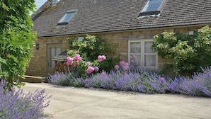 Ein Steinhaus mit geneigtem Dach, einer sichtbaren Treppe und einem Garten mit violetten Blumen.