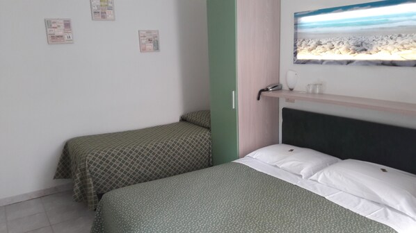 A room with two beds, a green wall, a window with a beach view, and a shelf with a phone and a glass. - Hotel Mariani (Camaiore)