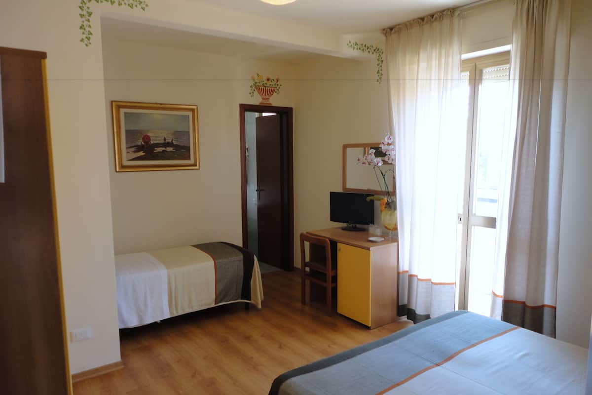 A hotel room with two beds, a desk with a computer, a painting on the wall, and a window with curtains.