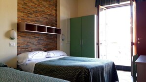 Ein Zimmer mit zwei Betten, einer Wand mit Ziegeloptik, einem grünen Kleiderschrank und einer Tür zum Ausgang.