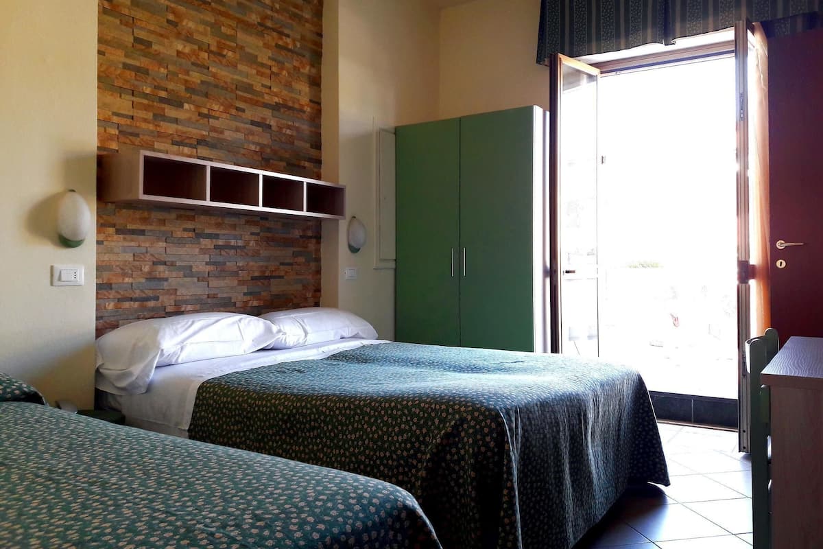 A room with two beds, a brick-patterned wall, a green wardrobe, and a door leading outside.