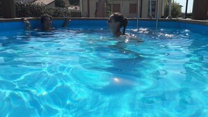 Ein Schwimmbad mit klarem, blauem Wasser, umgeben von einer Poolterrasse mit Fliesen und einem Gebäude im Hintergrund.