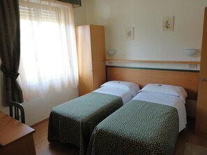 A hotel room with two single beds, a wooden headboard, a small table, and a chair. - Hotel Mariani (Camaiore)