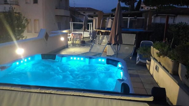 Ein Whirlpool mit Glasverkleidung und ein Poolbereich mit Liegestühlen und Sonnenschirmen.