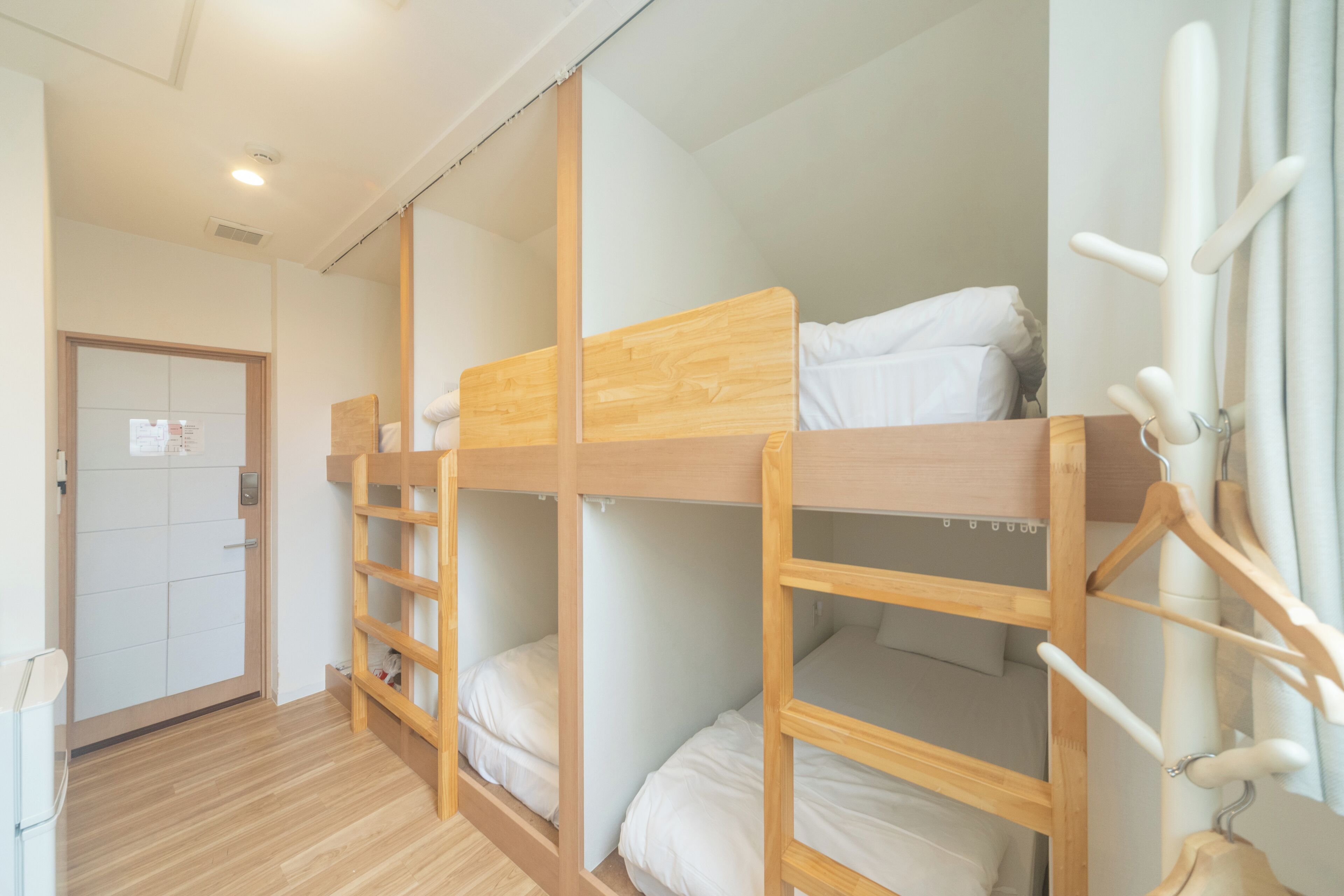 Dormitorio con literas de madera, una puerta con un aviso y un perchero.