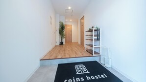 Um corredor com piso de madeira, uma porta no final e um tapete preto com o texto 'coins hostel'.