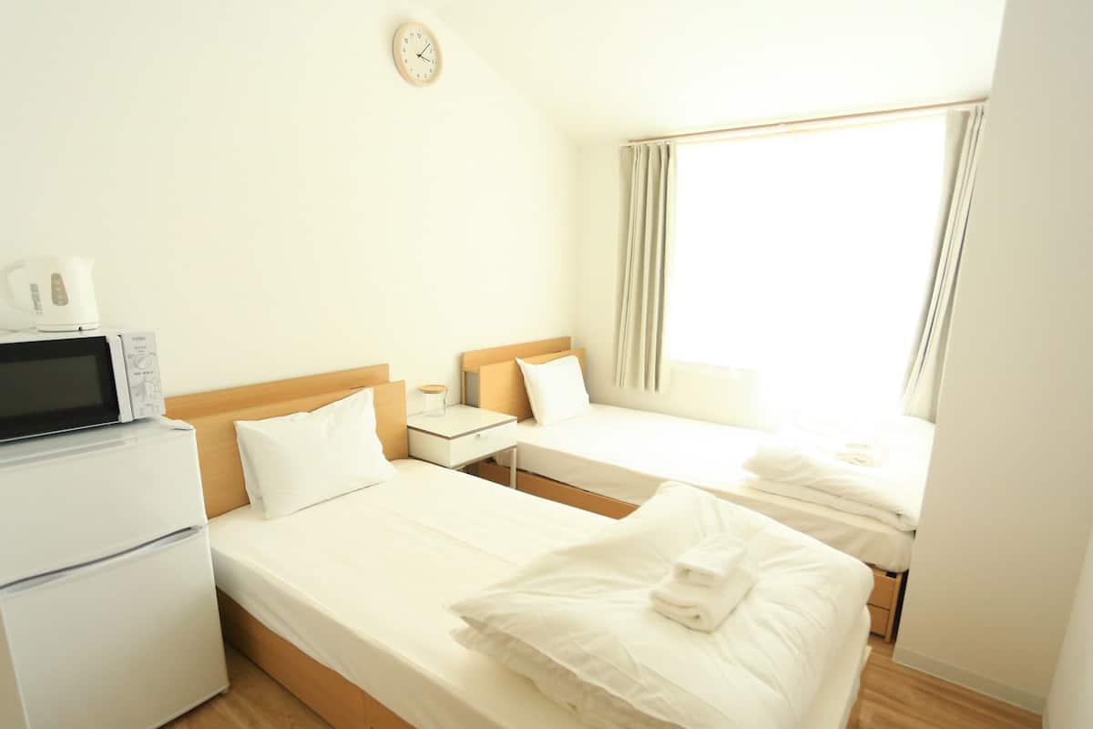 A hotel room with two beds, a microwave, a small table, and a clock on the wall.