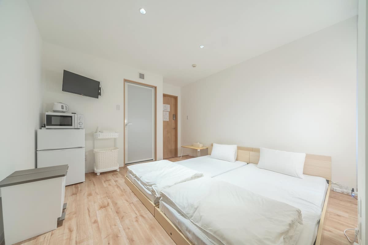 A hotel room with a bed, a desk, a microwave, a refrigerator, a TV, and a door.