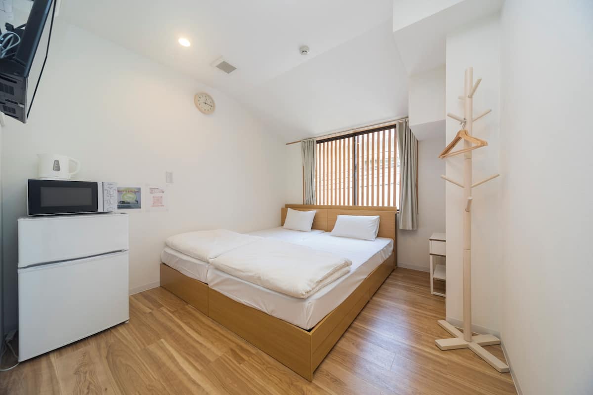 A bedroom with a bed, a white wardrobe, a microwave, a clock, and a coat rack.