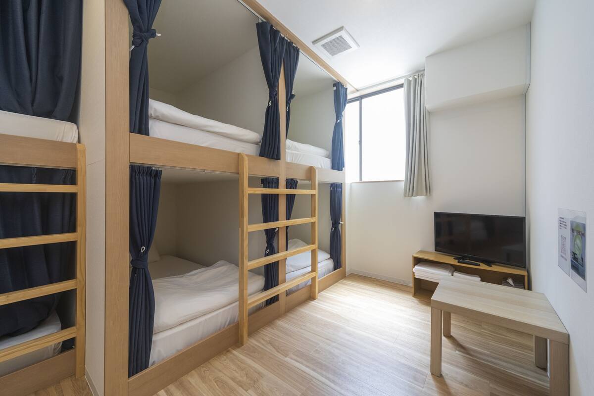 A bunk bed room with curtains, a TV, and a wooden bench.