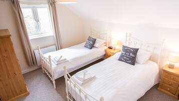 A bedroom with two single beds, a wooden wardrobe, a window with curtains, and bedside lamps.